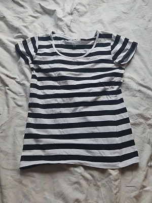Randig svartvit t-shirt - Snygg t-shirt med svartvita horisontella ränder och rund halsringning. Klassisk passform och korta ärmar, perfekt till jeans eller shorts. Tillverkad i mjuk bomull för skön känsla hela dagen.