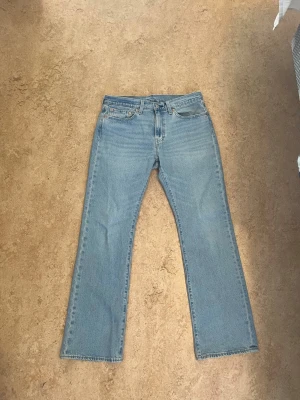 Levis 527 - Säljer ett par klassiska ljusblå jeans med bootcut passform och fem fickor. Jeansen har normal midja, dragkedja och knapp framtill samt detaljerade sömmar. Perfekta för en avslappnad och trendig look.