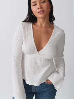 Vit långärmad topp med v-ringning - Trendig vit topp med djup v-ringning och långa ärmar. Tillverkad i ett lätt strukturerat tyg som ger en snygg och modern look. Perfekt att matcha med jeans eller kjol för en stilren outfit.