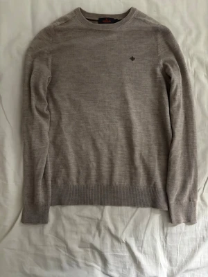 Beige morris tröja i merinoull - Snygg beige tröja med rund halsringning och diskret broderad logga på bröstet. Tröjan är tunnstickad i merinoull vilket gör tröjan väldigt skön. Tröjan är storlek Small och i mycket bra skick. Pris 699kr.