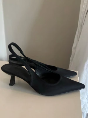 Svarta slingback pumps - Stilrena svarta pumps med spetsig tå och öppen häl i slingback-modell. Helt nya