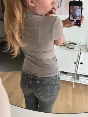 Grå low waist bootcut jeans - Säljer ett par grå low waist jeans med bootcut passform. Jeansen har klassiska fem fickor, slitna detaljer och en tvättad look. Perfekta för dig som gillar en avslappnad och trendig stil. De är lite uppgångna längst ned och uppsydda i butik. Inget som man tänker på. 