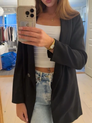 Svart oversized kavaj - Stilren svart oversized kavaj med enkelknäppning och klassisk krage. Långa ärmar och rak passform ger en trendig look. Perfekt att slänga över en crop top och jeans för en cool outfit.