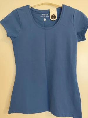 Blå basic t-shirt från No365 - En enkel blå t-shirt från No365 med rund halsringning och korta ärmar. Tillverkad i mjuk bomull som känns skön mot huden. Perfekt att matcha med jeans eller shorts för en clean och avslappnad look.
