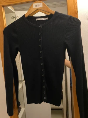 Svart ribbad kofta från 157 - Säljer en svart ribbad kofta från 157 med rund halsringning och knappar hela vägen framtill. Koftan har lång ärm och är tillverkad i ett stretchigt material som sitter snyggt på kroppen. Passar storlek xs/s💕
