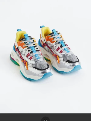 Buffalo färgglada chunky sneakers, stl 41 - Buffalo sneakers med chunky sula i vitt, blått och grönt. Ovandelen är i silverfärgat mesh och syntet med detaljer i orange, gult, rosa och blått. Insidan är gul och skorna har färgglada snören och logotaggar. Perfekta för dig som gillar statement-skor. Stl 41, änvända för fotografering bara 