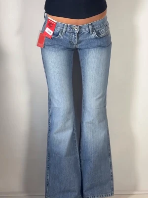 Ljusblå bootcut jeans med låg midja - Snygga ljusblå jeans med bootcut-modell och låg midja. Jeansen har klassiska fem fickor. Perfekta för dig som gillar en retro vibe och vill ha ett par jeans som sticker ut lite extra.