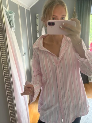 Rosa och vit randig oversized skjorta - Säljer en oversized skjorta i ljusrosa med vita och tunna gröna ränder. Skjortan har klassisk krage, knäppning framtill och långa ärmar. Perfekt för en chill och avslappnad stil.
