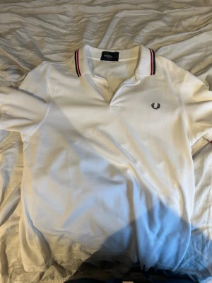 Vit pikétröja från Fred Perry - Klassisk vit pikétröja från Fred Perry med slim fit-passform. Tröjan har korta ärmar, krage med röda och marinblå ränder samt den ikoniska Fred Perry-loggan broderad på bröstet. Perfekt till både jeans och shorts. Riktigt bra skick då jag nästan aldrig använt den Nypris:1099, mitt pris:599. Priset kan diskuteras. Större chans att det blir billigare vid snabb affär 