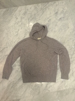 Sayless cashmere hoddie  - En stilren ljusgrå cashmere  hoodie. Andvänd typ 5 gånger! Tillverkad i ett mjukt, stickat material som känns skönt mot huden. Hoodien har långa ärmar och ribbade muddar vid ärmslut och nederkant. Perfekt för en avslappnad look.