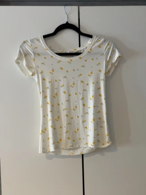 Vit t-shirt med citronmönster XS - Söt vit t-shirt med små gula citroner tryckta över hela plagget. Aldrig använd. T-shirten har rund halsringning och korta ärmar. Perfekt för dig som gillar fräscha och lekfulla prints. Tillverkad i mjuk bomull för skön känsla.