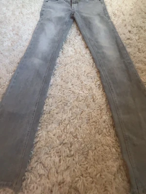 Ljusgrå raka jeans - Säljer ett par ljusgrå jeans med rak passform och klassisk femficksdesign. Jeansen har diskreta slitningar och är tillverkade i denim. Perfekta för dig som gillar en enkel och stilren look.