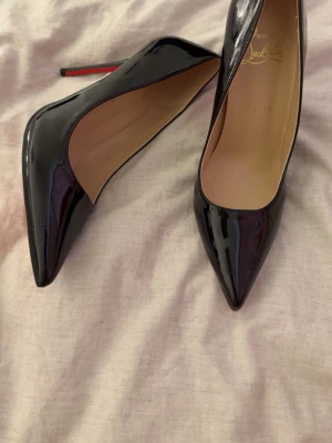 Svarta lackpumps från Louboutin - Säljer ett par klassiska svarta pumps i lack från Christian Louboutin med ikonisk röd sula och spetsig tå. Skorna har hög klack och elegant siluett, perfekta för att lyfta vilken outfit som helst. Väldigt små i storleken passar ej mig därför jag säljer, skickar med en dustbag då jag inte hittar den andra