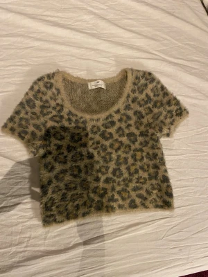 Leopardmönstrad fluffig kortärmad tröja - Säljer en supermjuk och fluffig kortärmad tröja med leopardmönster i beige och mörkbruna toner. Tröjan har rund halsringning och är croppad i modellen, perfekt för dig som vill sticka ut lite extra.