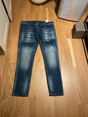Blå slitna jeans från Dsquared2 - Säljer ett par blå jeans från Dsquared2 med snygga slitningar och tvättade detaljer. Jeansen har smal passform och klassisk femficksdesign. Perfekta för dig som gillar en trendig och avslappnad stil.