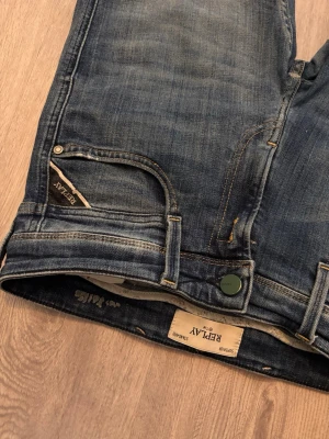 Blå jeans från Replay - Säljer ett par klassiska blå jeans från Replay med snygg tvätt och slitningar. Jeansen har fem fickor, Replay-logga på fickan och patch bak i midjan. Rak passform och detaljerade sömmar ger en tidlös look.