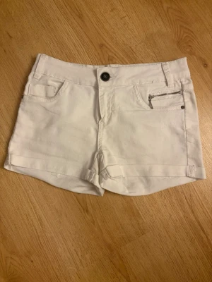 Vita shorts med dragkedjedetalj - Söta vita och ganska korta shorts med en liten dragkedjedetalj på fickan framtill. Klassisk femficksmodell med knapp och bälteshällor. 