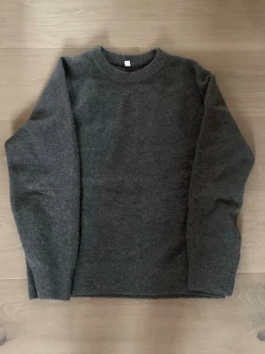 Mörkgrå stickad tröja från Uniqlo - Mysig mörkgrå stickad tröja från Uniqlo i storlek L. Tröjan har rund halsringning, långa ärmar och ribbstickade muddar vid ärmslut och nederkant. Tillverkad i mjukt material som passar perfekt för kyliga dagar.