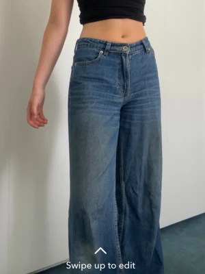 Blåa wide jeans med midwaist midja - Säljer ett par blåa jeans med midwaist midja och wide fit. Jeansen har klassisk femficksdesign, raka ben och stängs med knapp och dragkedja. Perfekta för en avslappnad och trendig look. Har sytt in de vid midjan så de sitter lite tajtare. 