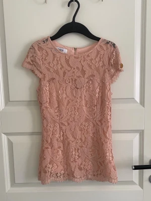 Rosa spetsblus med kort ärm - Supersöt rosa blus i spets med blommigt mönster och rund halsringning. Blusen har korta ärmar och dragkedja i ryggen. Perfekt att styla med jeans eller kjol för en trendig look.