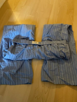 Blåa byxor med vita ränder - Snygga och bekväma byxor i blått med tunna vita ränder. Byxorna har resår i midjan och är tillverkade i ett lätt och mjukt tyg, perfekt för att chilla hemma eller dra på sig en sen sommarkväll. Klassisk rak passform och tidlös design.
