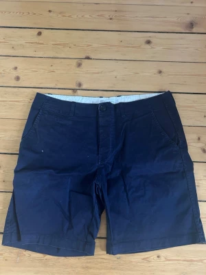 Mörkblå shorts från Samsøe Samsøe - Snygga mörkblå shorts från Samsøe Samsøe i klassisk modell med raka ben och knappgylf. Tillverkade i ett mjukt bomullstyg med sidofickor och bälteshällor. Perfekta för varma dagar och enkel att matcha med olika stilar.