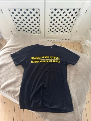 AIK T-shirt  - AIK t-shirt med trycket 'Rädda svensk fotboll, skrota villkorstrappan' i gult på bröstet. Klassisk passform med rund hals och korta ärmar. Perfekt för dig som vill visa ditt stöd för svensk fotboll. Går ej att få tag på längre