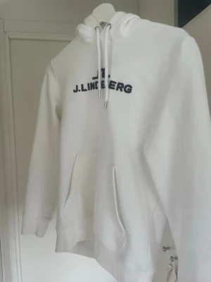 Vit hoodie från J.Lindeberg - Säljer en clean vit hoodie från J.Lindeberg med svart logga på bröstet. Hoodien är knappt använd!