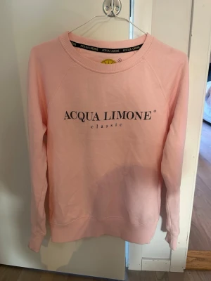 Ljusrosa sweatshirt Acqua Limone - En jättefin ljusrosa sweatshirt från Acqua limone med klassisk logga tryckt på bröstet. Tröjan har även en  rund halsringning, ribbade muddar och  tillverkad i ett mjukt bomullsmatrial. Nypris 1099 kr. 