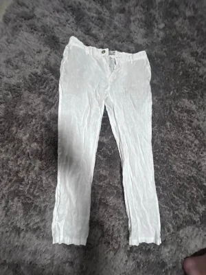 Vita linnebyxor från Dressmann - Snygga vita linnebyxor från Dressmann i 100% linne. Byxorna har rak passform, knapp och dragkedja framtill samt hällor för bälte. Perfekta för en avslappnad och stilren look under varma dagar.