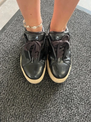 Svarta eytys  - Snygga svarta sneakers från eytys med glansig finish och tjock vit sula. Skorna har svarta skosnören och en klassisk låg design som passar till allt. Vill bara bli av med dom så buda på!