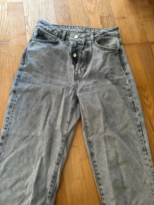 Gråa vida jeans med hög midja - Säljer ett par gråa jeans med hög midja och raka, vida ben. Jeansen har klassisk femficksmodell och stängs med knapp och dragkedja. Materialet är denim i 100% bomull och färgen är tvättad grå för en cool vintagekänsla. W28 L32