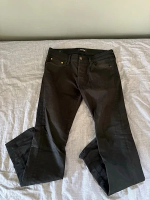 Jack&Jones slim Glenn - Säljer ett par svarta slim jeans med klassisk femficksdesign och knappgylf. Jeansen har raka ben med lätt utsvängning nedtill och är tillverkade i ett mjukt denimtyg. Perfekta för dig som gillar en tidlös och clean look.