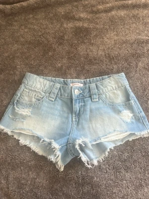 Ljusa jeansshorts med fransig kant - Säljer ett par jättefina ljusblå low waist jeansshorts med fransig kant och slitna detaljer framtill från Gina tricot. Kommer tyvärr inte till användning då de är för stora. Är storlek xs men är ganska stora i storleken.