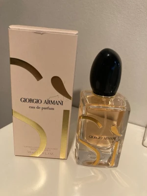 Giorgio Armani Sì Eau de Parfum 50ml - Giorgio Armani Sì Eau de Parfum i elegant glasflaska med svart kork och guldiga detaljer. Parfymen har en stilren design och kommer i en ljusbeige kartong med guldmönster. Perfekt för dig som gillar lyxiga dofter. Använd vid fåtal tillfällen. 
