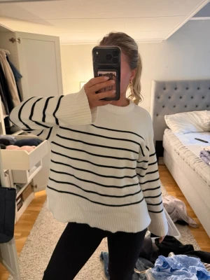 Vit stickad tröja med svarta ränder - Säljer en oversized vit stickad tröja med svarta horisontella ränder. Tröjan har rund hals, långa ärmar och breda ribbade muddar vid ärmslut och nederkant. Perfekt för en avslappnad och trendig look.