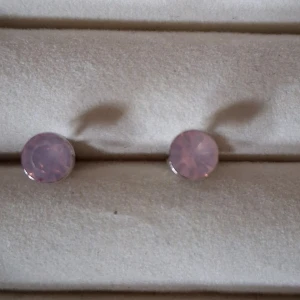 Rosa studsörhängen i silverfärg - Säljer ett par studsörhängen med ljusrosa, facetterade stenar infattade i silverfärgad metall. Diameter ca 6 mm. Nya och oanvända men saknar prislapp och förpackning.