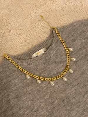 Guldfärgat halsband med pärldetaljer - Snyggt halsband i guldfärgad metall med kedja och hängande vita pärlor. Perfekt för att ge din outfit en trendig touch. Kedjan har en klassisk design och pärlorna ger en elegant kontrast.