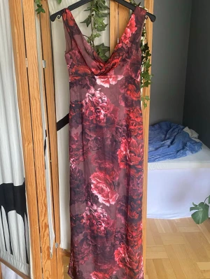 Långklänning med blommor xs/s - Säljer en elegant långklänning med stora blommor i rött och rosa på mörk botten. Inga tecken på användning. Står xs men skulle snarare säga att den sitter som s.