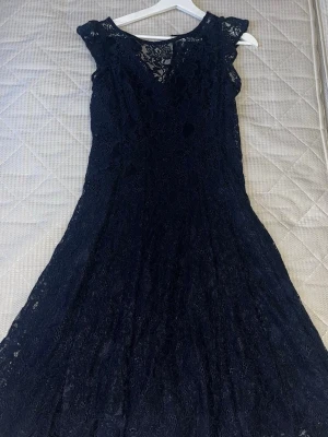 svart klänning i spets - Säljer en elegant svart klänning med v-ringning och spetsdetaljer. Klänningen har korta ärmar och är helfodrad med ett vackert fall. Perfekt för dig som vill ha en klassisk och stilren look.