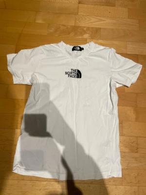 Vit t-shirt från The North Face - Säljer en klassisk vit t-shirt från The North Face med logga tryckt på bröstet. T-shirten har rund halsringning och korta ärmar. Tillverkad i mjuk bomull som är skön att bära hela dagen.