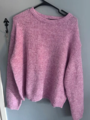 Oversized lila stickad tröja - Mysig oversized stickad tröja i lila med rund halsringning och långa ärmar. Tröjan har en enkel design utan mönster och är stickad i ett mjukt material som känns skönt mot huden. Perfekt för kyliga dagar när du vill vara både bekväm och snygg.