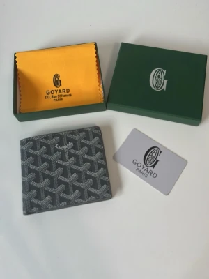 Grå g plånbok i läder - Snygg grå plånbok från G med det klassiska mönstret och flera kortfack. Tillverkad i läder och levereras med originalask, tygpåse och äkthetskort. Perfekt för dig som vill ha något exklusivt och stilrent i fickan.