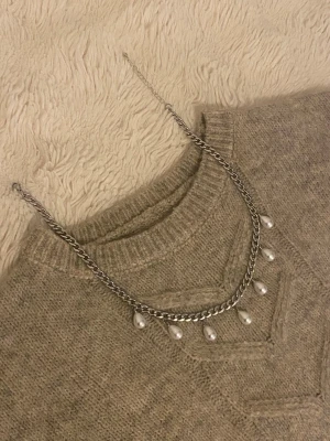 Silverfärgat halsband med pärldroppar - Snyggt halsband i silverfärgad rostfritt med sju droppformade vita pärlor som hänger längs kedjan. Perfekt för att ge en elegant touch till din outfit. Kedjan har en klassisk design och pärlorna ger en trendig vibe.
