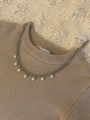 Silverfärgat halsband med pärlor - Snyggt halsband i silverfärgad rostfritt med kedja och hängande vita pärlor. Kedjan har en chunky känsla och pärlorna ger en elegant touch. Perfekt accessoar för att lyfta din outfit med en mix av stilrent och trendigt.