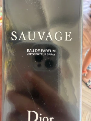 Sauvage Eau de Parfum från Dior - Sauvage Eau de Parfum från Dior i en elegant mörk glasflaska med svart lock. Doften är intensiv och maskulin, perfekt för dig som gillar exklusiva parfymer. Flaskan har en stilren design med tydlig logga och text i vitt.