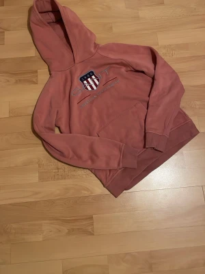 Rosa hoodie från Gant med tryck - Säljer en rosa hoodie från Gant med broderad logga och text på bröstet. Hoodien har en stor huva, magficka och ribbade muddar vid ärmslut och nederkant. Perfekt för en avslappnad och snygg stil. Jag har använt hoodie ett fåtal gånger och det är väldigt bra skick, hör av er vid frågor eller om ni vill diskutera priset🙂