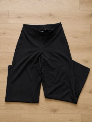 Svarta utsvängda byxor Gina Tricot M - Svarta utsvängda byxor från Gina Tricot i mjukt och stretchigt material. Byxorna har hög midja och är tillverkade i en blandning av polyester och elastan för en bekväm passform. Lite nopprig. Benlängd: 80cm