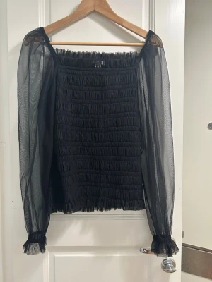Svart meshblus med puffärmar från ARKET - Trendig svart blus från ARKET med smockad kropp och transparenta meshärmar. Puffiga långärmar med resår vid handlederna ger en snygg siluett. Perfekt för dig som vill ha en statement topp med coola detaljer.