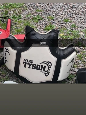 Boxningsskydd Mike Tyson svart/vit - Säljer ett boxningsskydd i svart och vitt med tydlig Mike Tyson-logga framtill. Skyddet har vadderade partier och är designat för att absorbera slag vid träning. Perfekt för sparring och boxningspass.